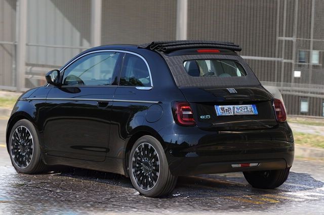 Rear view of a black compact hatchback car parked on a wet road near an industrial building.