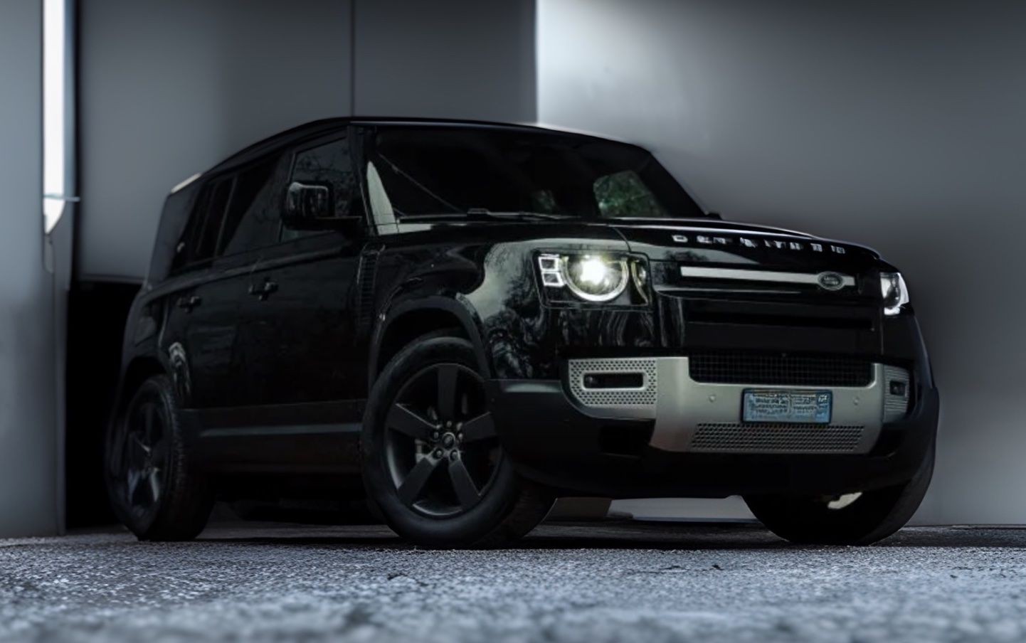 Black SUV with illuminated headlights parked in a garage, shown from the front angle.