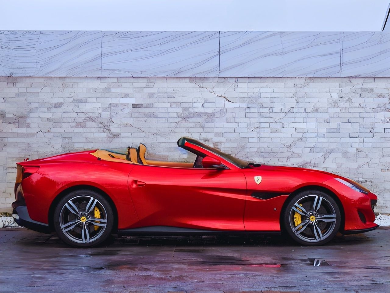 Side view of a red sports convertible car parked in front of a brick wall.